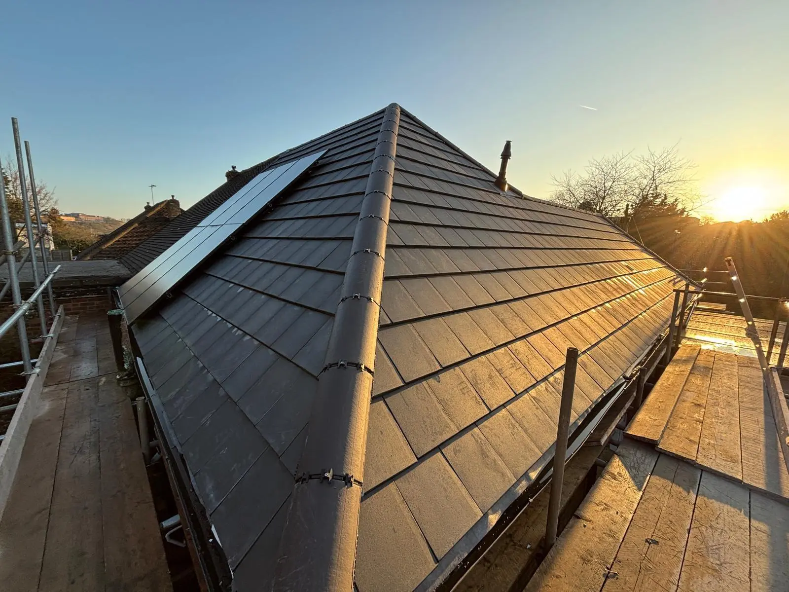 Newly tiled grey hip roof with solar panels, finished at sunset